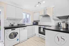 Una cocina moderna con armarios blancos, lavadora integrada, microondas y hervidor.