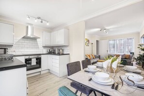 Una cocina moderna con armarios blancos, horno empotrado y comedor con mesa para seis comensales.