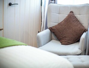 Una silla con un cojín marrón, una puerta blanca con un picaporte negro, y una manta verde en el suelo.