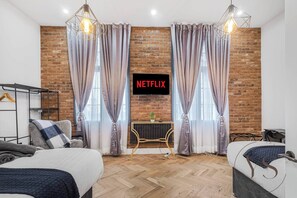Quarto de hotel moderno com parede de tijolos, televisão exibindo 'NETFLIX', piso de madeira e cama com cabeceira.