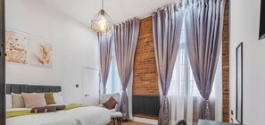 Un dormitorio con cama, un radiador, una lámpara colgante y una pared de ladrillo.