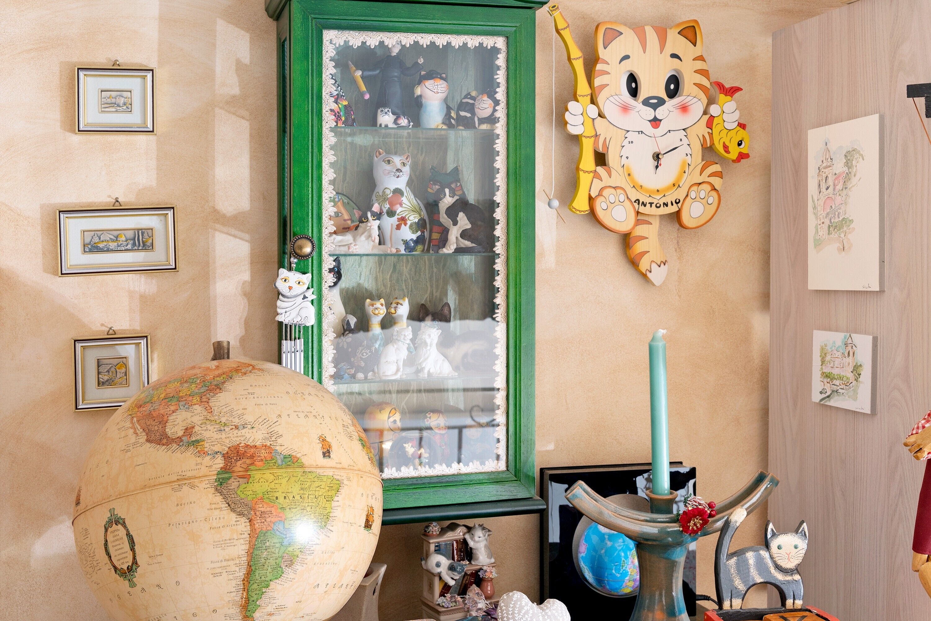 Une pièce comprenant un globe terrestre, des tableaux encadrés, un meuble vert orné de statuettes et une décoration représentant un tigre.