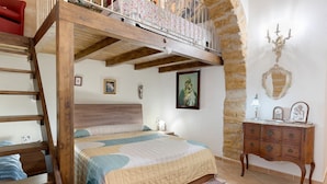 Ein Schlafzimmer mit einem Holzbettgestell, einem Bett mit Patchworkdecke, einem Schminktisch und einem an der Wand befestigten Spiegel.