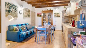 Ein gemütliches Wohnzimmer mit einem blauen Sofa, einem Holzespeisetisch und Stühlen. Es gibt eine Küchenzeile mit Schränken und einer Mikrowelle.