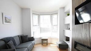 En moderne stue med en grå sofa, et lille bord og et tv monteret på væggen med en sort ramme.