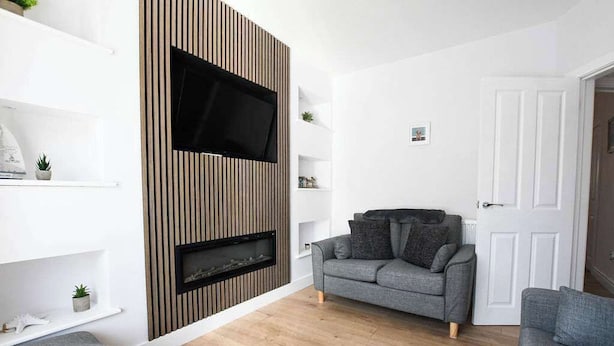 En moderne stue med et fladskærms-tv, en pejs, grå sofaer og hvide reoler.