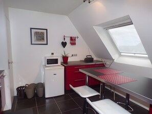 A compact kitchen with a microwave, a small refrigerator, a red countertop, a window with blinds, and a ceiling fan.