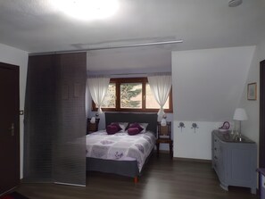 A bedroom with a bed, a nightstand, a dresser, a window with curtains, and a door.