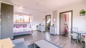 Ein modernes, gut beleuchtetes Zimmer mit einem Bett, einem Schreibtisch, einem Sessel und einem kleinen Tisch.
