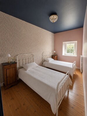A bedroom with two single beds, a wooden cabinet, a nightstand, a window with a view, and a decorative ceiling light. - Vrbo Property (Vervant)