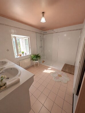 A bathroom with a shower, two sinks, a window, and a radiator. - Vrbo Property (Vervant)