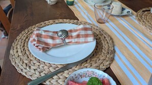 A wooden dining table with a placemat, a plate with a checkered napkin, a bowl of watermelon, and a vase with flowers. - Charming suite near St Jean d'Angély (Vervant)