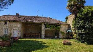 A stone building with a tiled roof, a covered outdoor seating area, and a grassy yard. - Charming suite near St Jean d'Angély (Vervant)