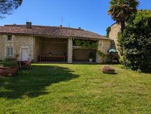 A stone building with a tiled roof, a covered outdoor seating area, and a grassy yard. - Vrbo Property (Vervant)