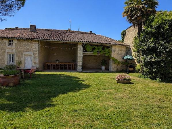 A stone building with a tiled roof, a covered outdoor seating area, and a grassy yard.