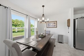 Eine moderne Küche mit Holztisch, einer Chandelüster, einem Kühlschrank und einem Fenster mit Blick auf Grünflächen.