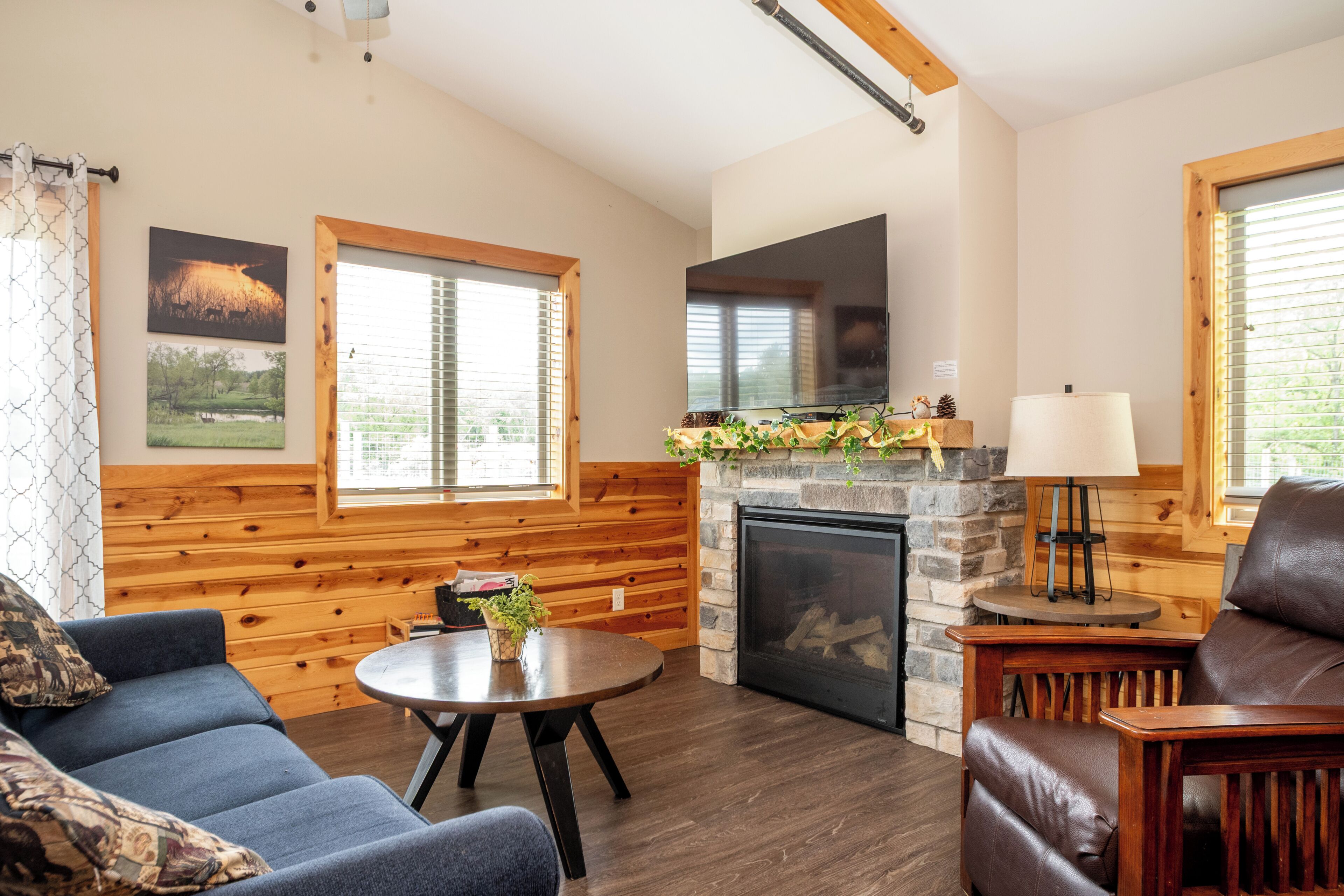 Interior acogedor de una cabaña con chimenea, paredes de madera, un sofá, una mesa y una lámpara.