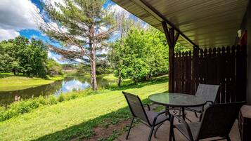 Une terrasse extérieure avec une table et des chaises, une vue sur un étang et une clôture en bois.