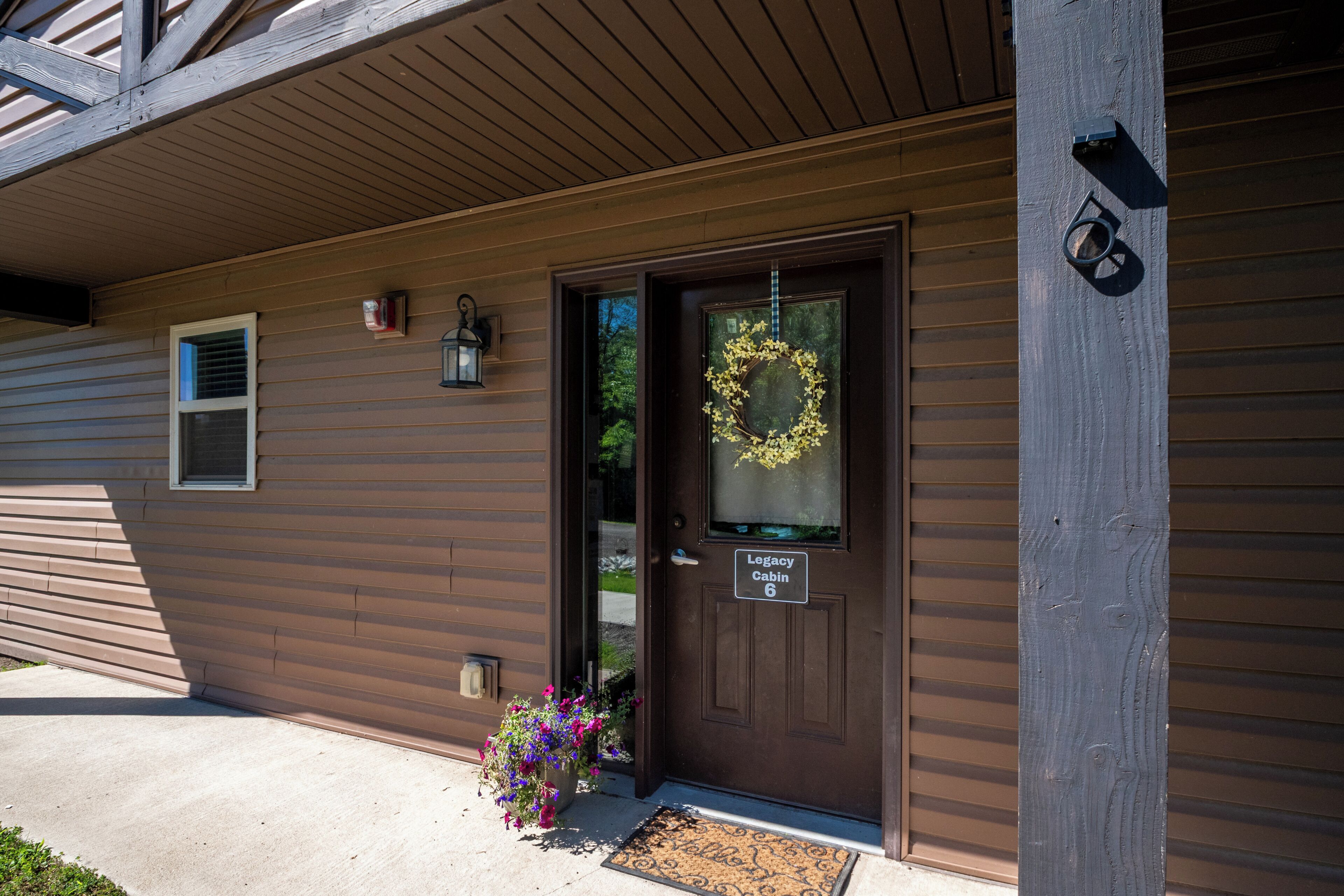 Une maison en bois brun avec une porte portant l’inscription « Legacy Cabin 6 ».
