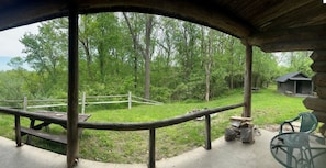A covered outdoor area with a picnic table, a chair, and a small cabin in the background.