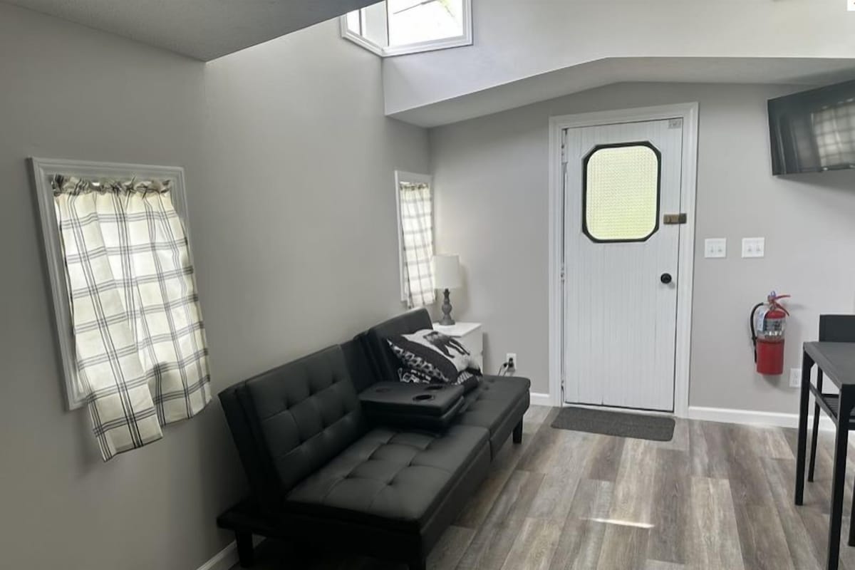 A living room with a sofa, a door, and a fire extinguisher.