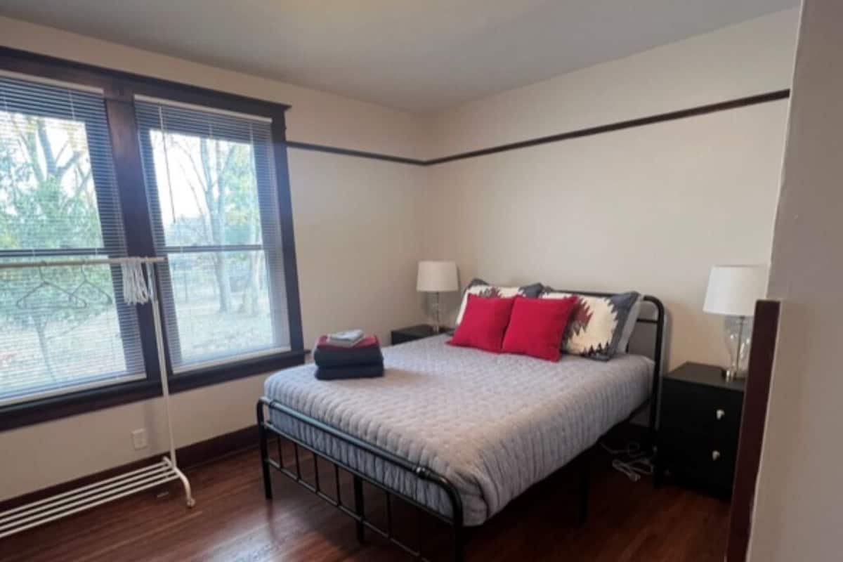 Un dormitorio con cama, mesitas de noche, una ventana y un radiador.