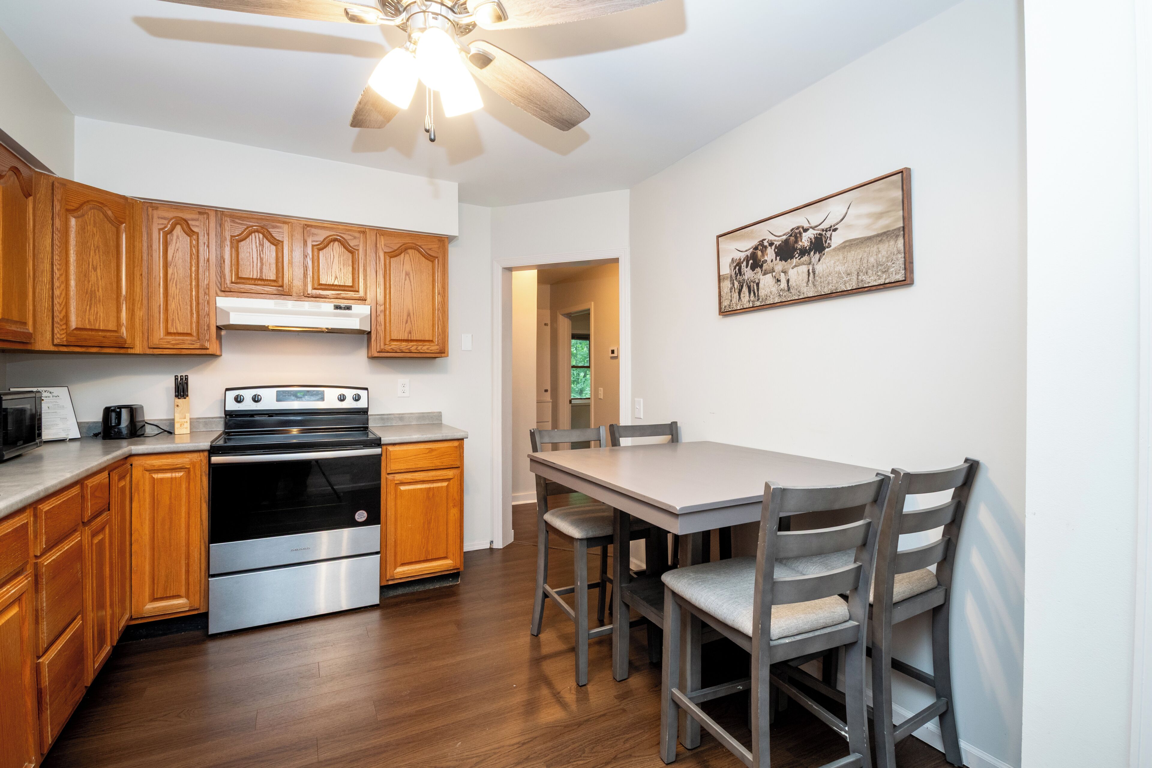 A kitchen with wooden cabinets, a stainless steel oven, a dining table with chairs, and a ceiling fan.