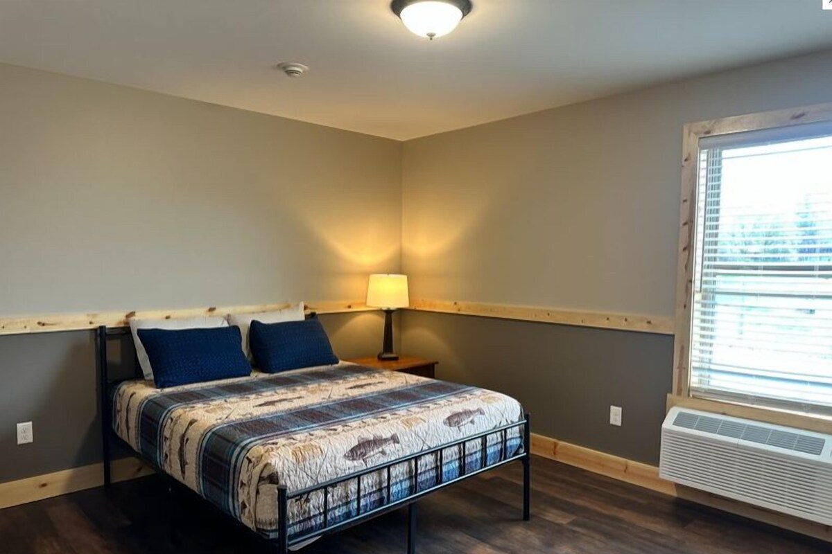 Un dormitorio con cama, mesita de noche, lámpara y ventana con persianas.