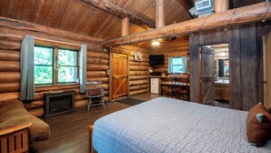 Interior de una cabaña de madera con cama, chimenea, comedor y cocina.