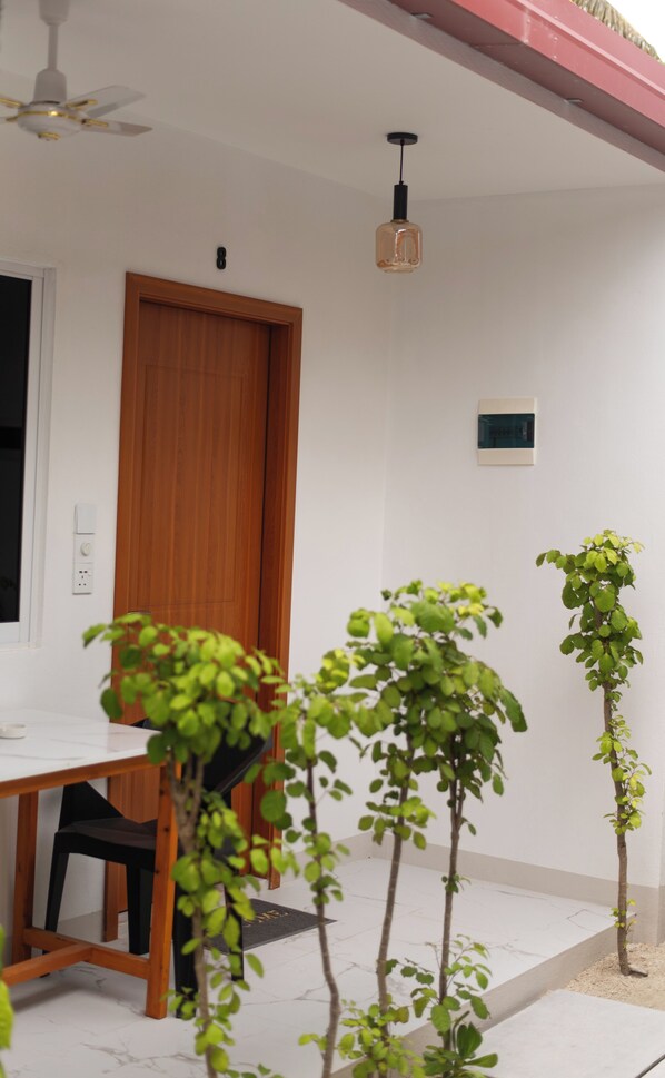 A room with a wooden door, a ceiling fan, a small table, and a potted plant. - Paradise Palms (Thoddoo)
