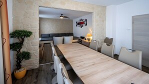 A modern room with a wooden dining table, a sofa, a TV, and a stone wall. - City Holiday Home Daun in Daun – for 14 Guests (210 m²) (Daun)