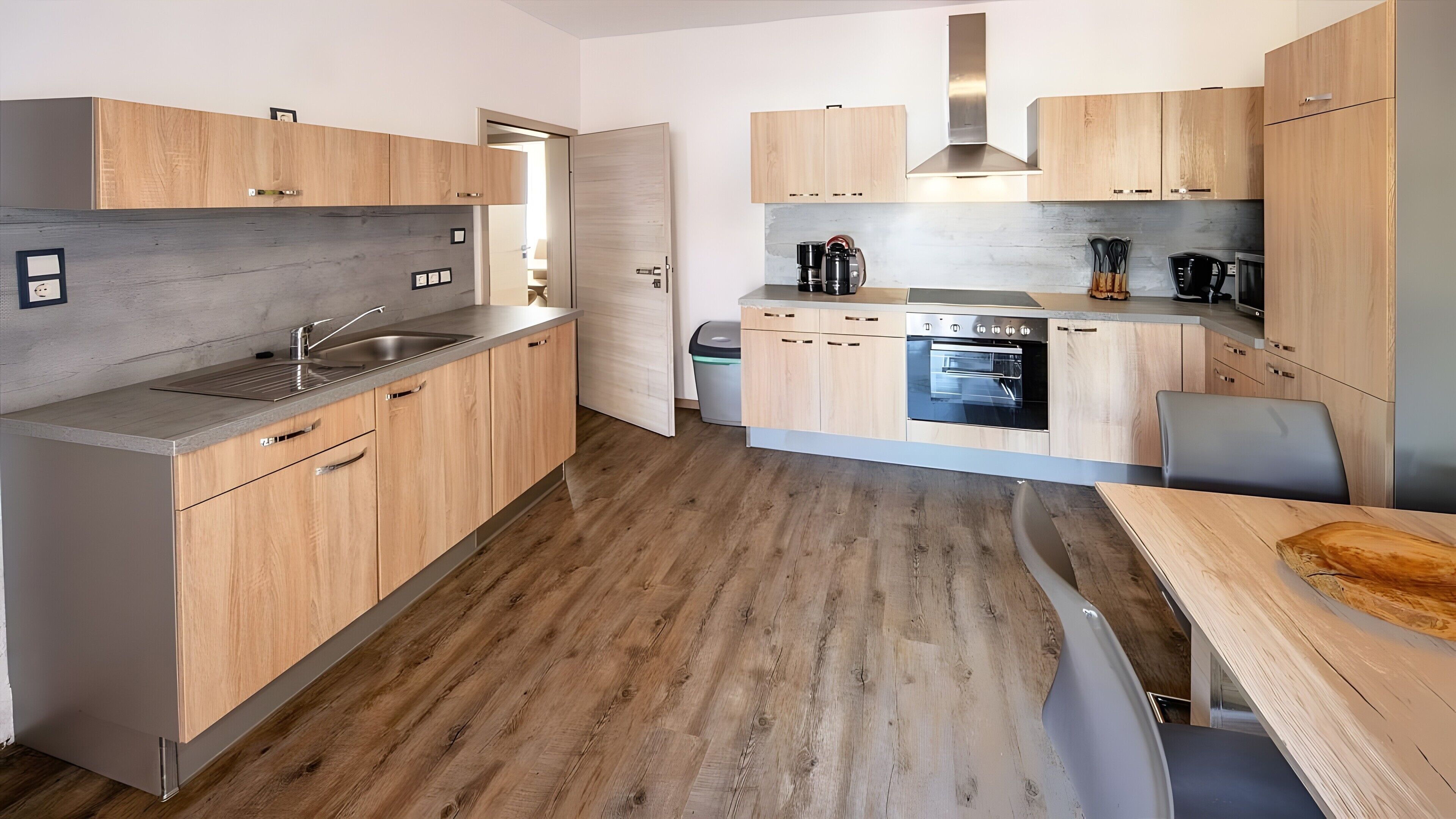 Una cocina moderna con armarios de madera, horno empotrado y pileta de acero inoxidable.