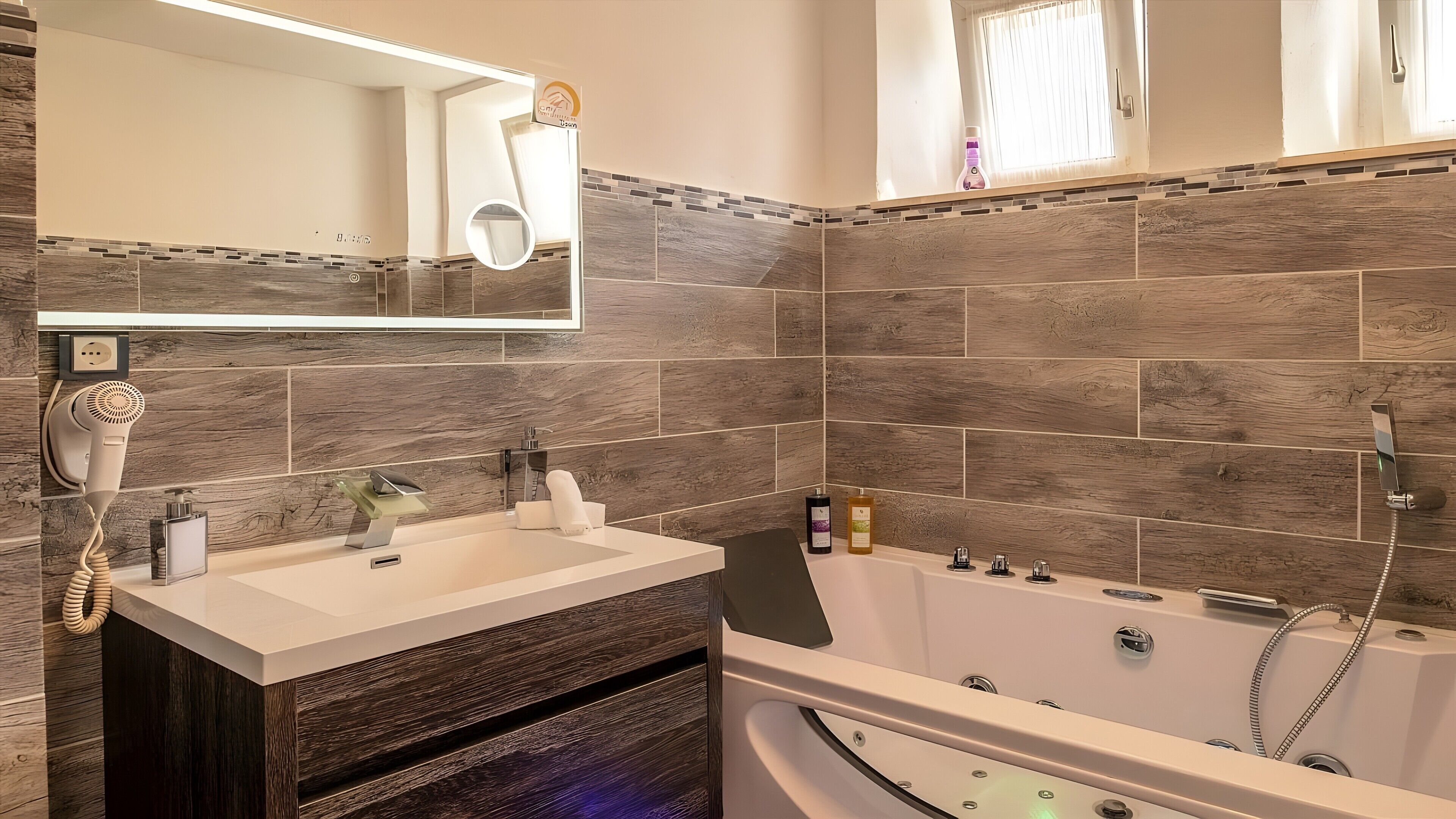 A modern bathroom with a built-in sink, a hairdryer, a mirror, a bathtub with multiple showerheads, and a window with curtains.