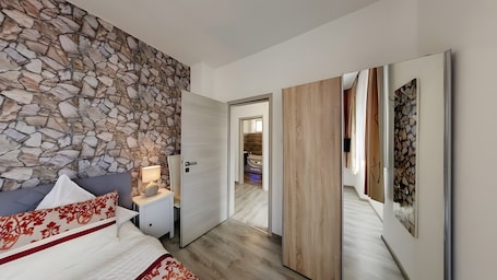 A bedroom with a stone wall, a bed with patterned pillows, a bedside table with a lamp, and a wooden door leading to a bathroom.. City Holiday Home Daun in Daun – for 14 Guests (210 m²)