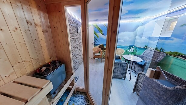 A wooden interior with a stone wall, a small seating area with a table and chairs, and a view of a beach through a glass door. - City Holiday Home Daun in Daun – for 14 Guests (210 m²) (Daun)