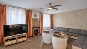 Ein modernes Wohnzimmer mit Flachbildfernseher, Kamin aus Stein, gebogenem Sofa und Deckenventilator.