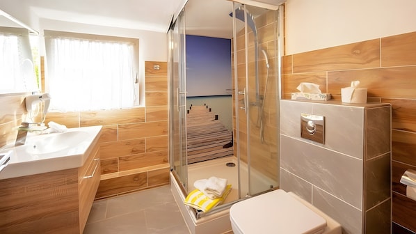 Ein modernes Badezimmer mit einer Duschkabine aus Glas, Holzboden und Blick auf eine Holzterrasse durch die Duschwand.
