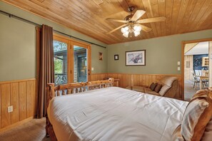 A bedroom with a large bed, wooden ceiling, and a view of the outdoors.