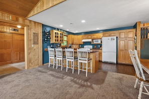A kitchen with wooden cabinets, a central island with chairs, a refrigerator, and a microwave.