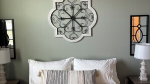 Een net opgemaakt bed met witte lakens, een decoratieve wandhanger en nachtlampjes.