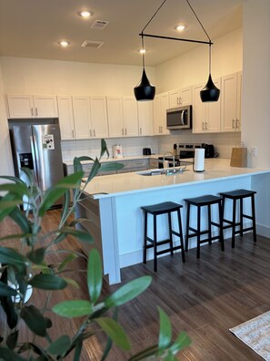 Una cocina moderna con armarios blancos, electrodomésticos de acero inoxidable y una isla central con taburetes de bar.
