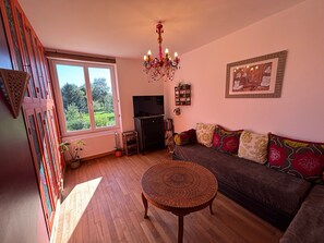 Ein Wohnzimmer mit einer Couch, einem Fernseher, einer Chandelier und einem Fenster mit Blick auf Grünflächen.