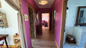 Un corridoio con pavimento in legno, un lampadario, un armadietto in legno e un televisore alla destra.