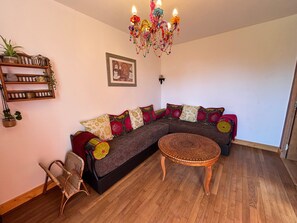 A living room with a sectional sofa, a wicker chair, a round wicker coffee table, a colorful chandelier, and a wall-mounted shelf with plants. - At Patricia's: A spacious townhouse in the countryside in Graçay (Graçay)