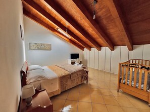 Een slaapkamer met een bed, een bureau, een stoel, een ledikant en een wandlamp.