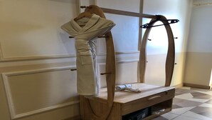 A wooden bench with a robe and towel hanging on a wooden rack, a wooden drawer, and a patterned floor. - Sunday Sky Hotel in Korean Town Angeles, Near Clark International Airport (Angeles City)