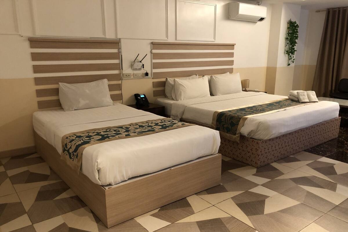 Dos camas con cabeceras, una mesita de noche con teléfono, aire acondicionado de pared y una alfombra estampada.