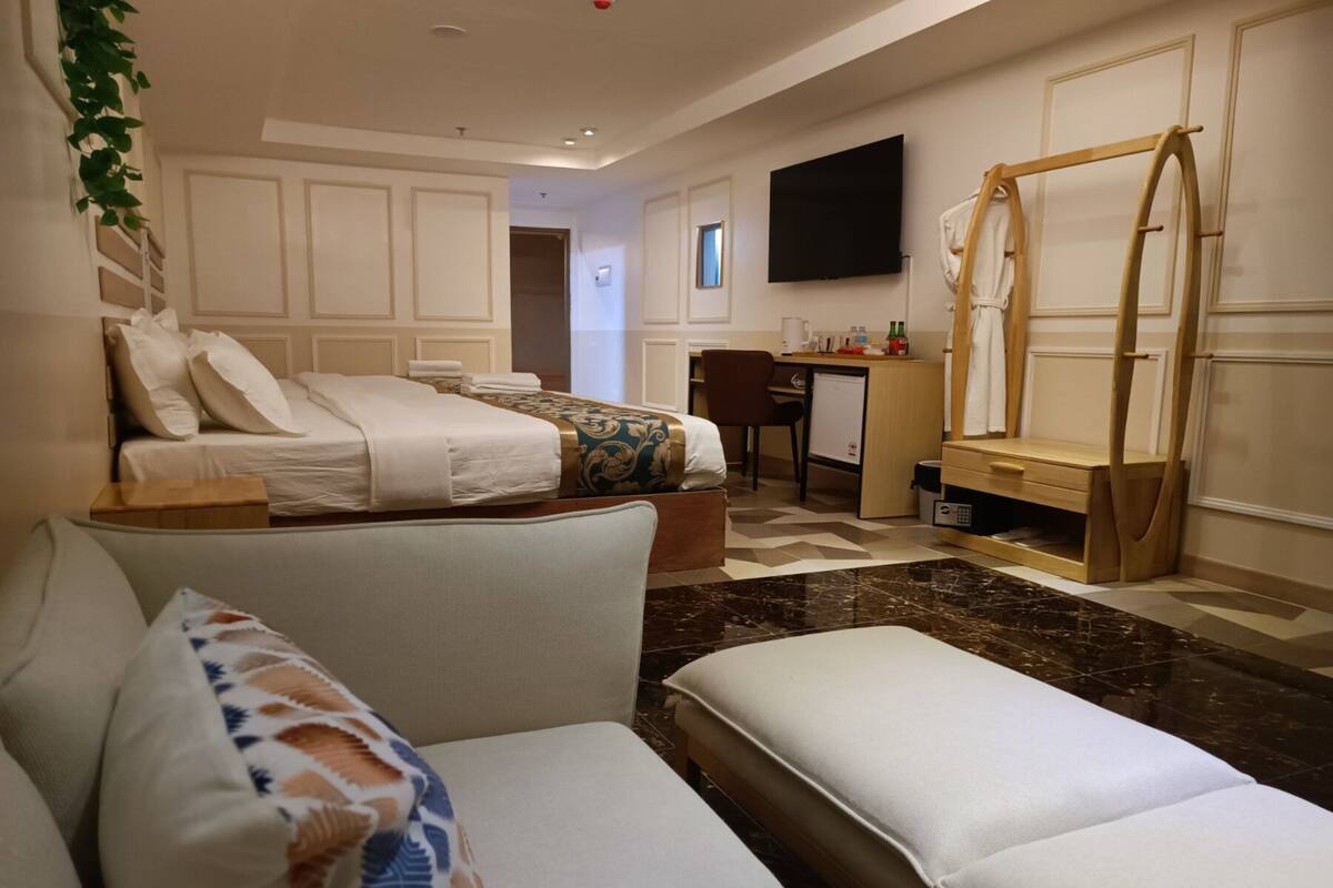Una habitación de hotel con cama, sofá, escritorio, televisor y un tendedero de madera.
