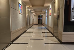 Un couloir d’hôtel avec un sol carrelé, des portes et des œuvres d’art encadrées accrochées aux murs.