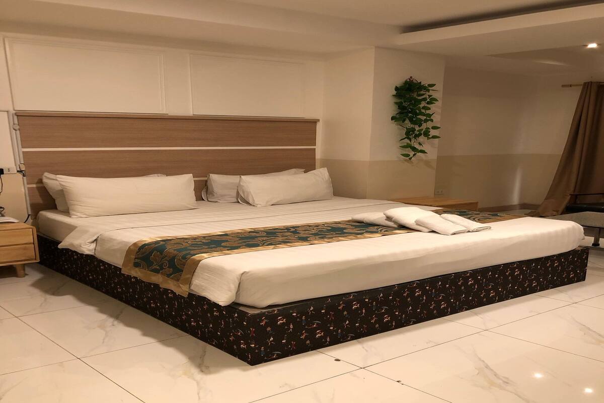 Una cama grande con cabecera de madera, un plaid decorativo y falda de cama estampada.